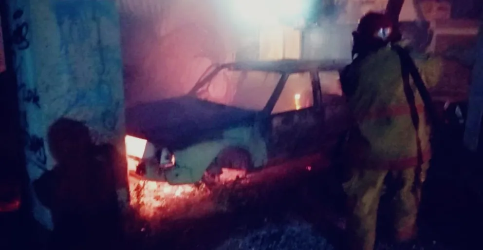 El vehículo quemado en el barrio Ceferino y los bomberos en plena actividad. 