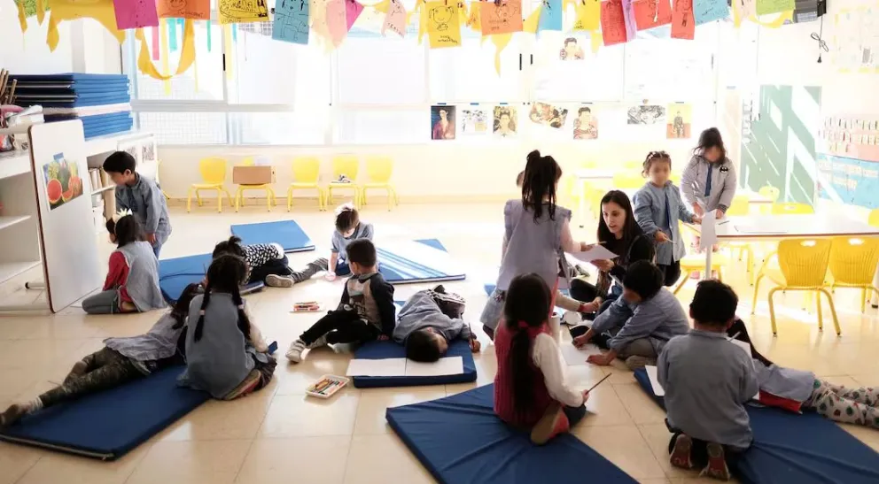 Hablar a la altura de los chicos, agacharse decenas de veces al día y acomodarse en un mobiliario pensado para niños esconde un desgaste corporal acumulativo. Foto: Web.