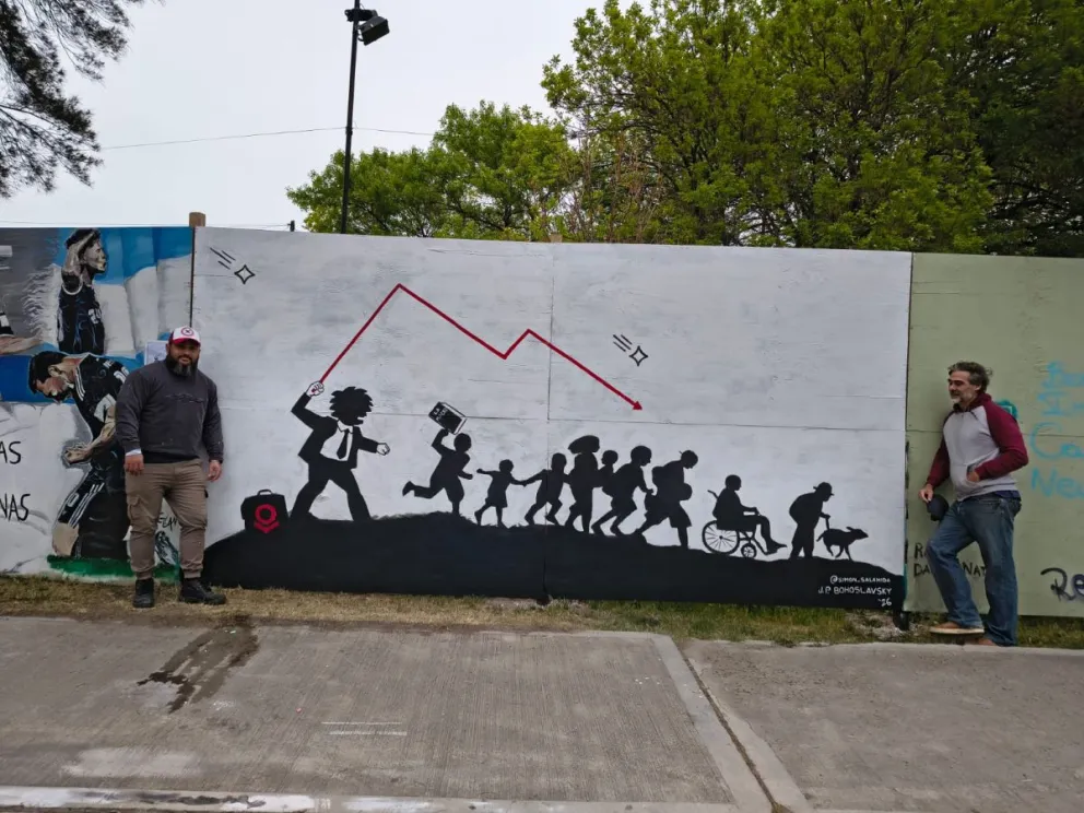Simón Salamida y Juan Pablo Bohos adaptaron una obra de Banksy para pintar un mural político en el vallado del Centro Cultural de Viedma. Foto: Gentileza.